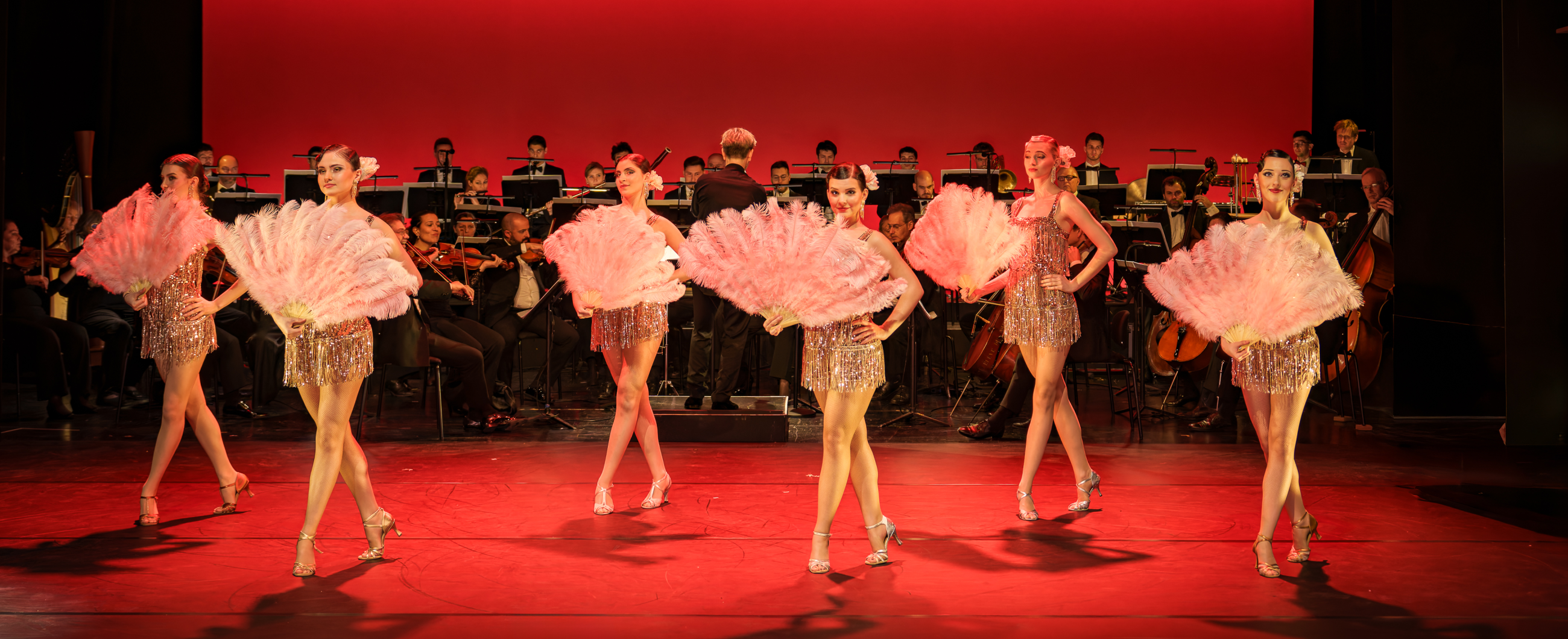 sechs Tänzerinnen mit Orchester im Hintergrund