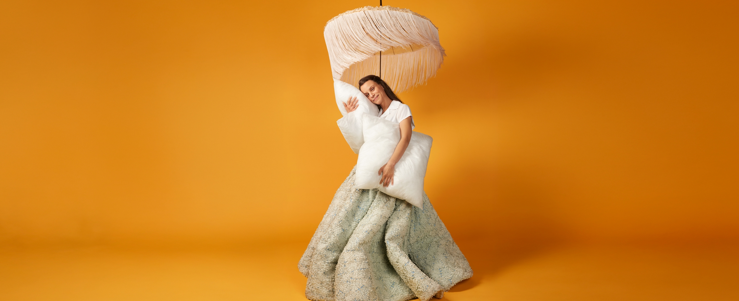 eine junge frau im flauschkleid mit kissen und fransenschirm